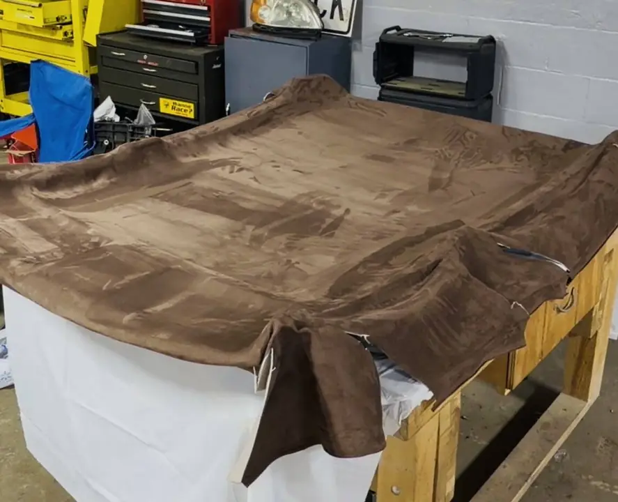 Brown suede headliner fabric laid out on the bench mid install