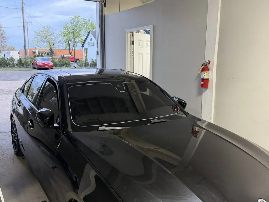 Ceramic film being laid onto a black sedan windshield in the Rook Auto Customs bay, shop doorway open behind