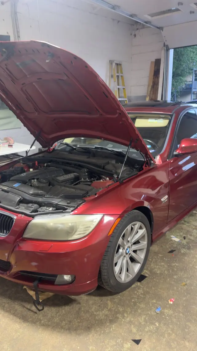 A red BMW 3-series with the hood raised inside the Rook Auto Customs shop bay
